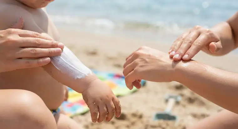 Stosowanie kremu z filtrem dla dzieci na plaży, równomierne rozprowadzanie ochronnej warstwy na skórze dziecka przed słońcem